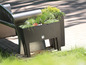 Un pot de fleurs brun avec différentes plantes sur une terrasse.
