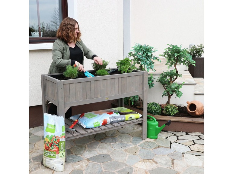 Une femme plante dans une jardinière en bois avec du terreau Blumerde.