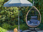 Un fauteuil suspendu avec un coussin et un parasol à franges dans un jardin.