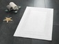 Un tapis de bain blanc avec une bordure décorative sur des carreaux