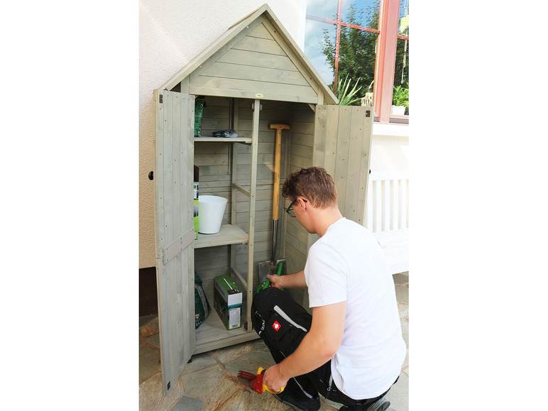 Un homme range des outils de jardinage dans un abri en bois.