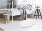 Un tapis blanc en fourrure devant un lit blanc à pois noirs.