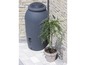 Un tonneau de pluie gris à côté d'une plante en pot.
