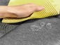 Une main essuie une éponge jaune sur un tissu imperméable.