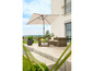 Un parasol beige avec un salon en osier sur une terrasse.