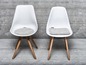 Deux chaises blanches avec des pieds en bois et des coussins en laine gris.