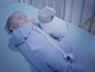 Un bébé en pyjama bleu regarde un agneau en peluche dans un berceau.