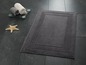 Un tapis de bain gris avec un bord décoratif sur un sol en carrelage.