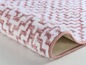 Un tapis de bain rose avec un motif géométrique blanc.