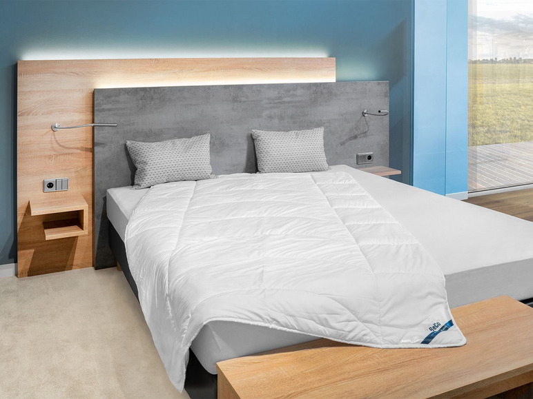 Une couette blanche de la marque Rössle sur un lit dans une chambre à coucher.