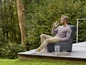Un homme assis sur un fauteuil gris de salon sur une terrasse en bois.