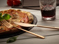 Une fourchette et un couteau en rose gold d'Echtwerk à côté d'une pizza et d'un verre de vin rouge.