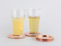 Deux verres avec du jus et du thé sur des dessous de verre en cuivre.