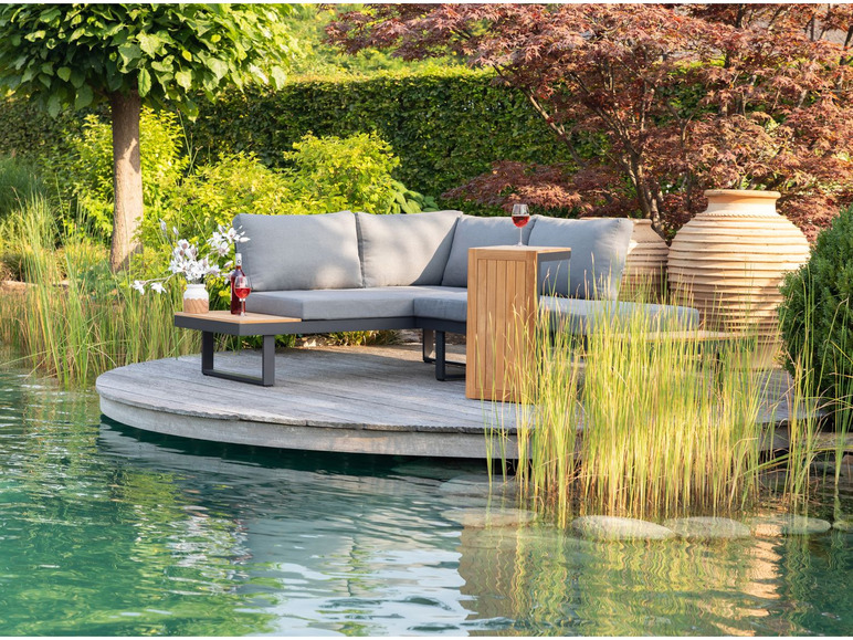 Un canapé d'angle gris avec une table basse en bois sur une terrasse en bois au bord d'un lac.