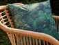 Un coussin à imprimé tropical sur une chaise en rotin.