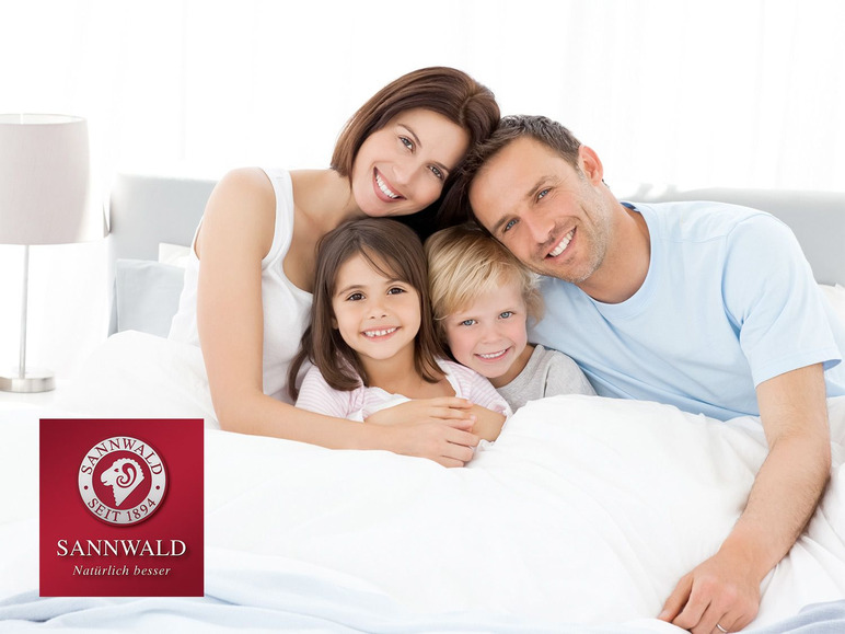 Une famille sourit dans un lit avec des draps Sannwald.