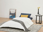Une couette blanche sur un canapé-lit avec une couverture grise et une table d'appoint.