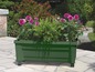 Une jardinière verte à roulettes, remplie de fleurs et de fougères.
