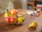 Un panier à fruits doré avec des bananes, des pommes, un pamplemousse, une mangue et une poire.
