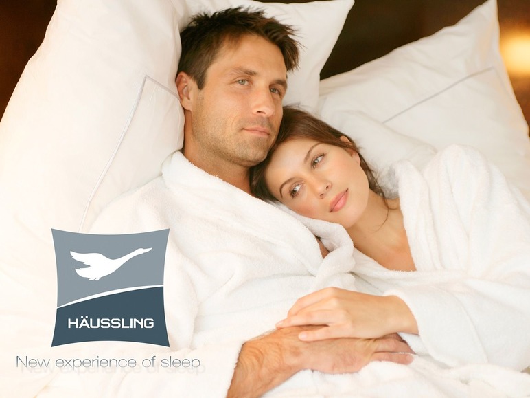 Un couple en peignoirs blancs dans un lit, avec le logo Häussling et le slogan 'Nouvelle expérience du sommeil'.
