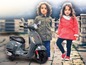 Deux enfants à côté d'une Vespa grise.