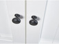 Deux boutons noirs sur une porte d'armoire blanche.