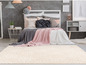 Un tapis beige avec un motif géométrique blanc devant un lit avec des couvertures roses et grises.