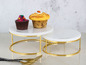 Deux plateaux ronds en marbre pour gâteaux avec un piétement doré, décorés de cupcakes.
