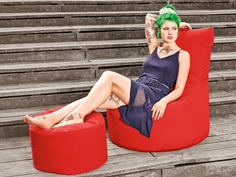 Une femme assise sur un fauteuil beanbag rouge avec un repose-pieds assorti.