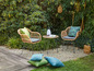 Deux chaises en rotin avec des coussins, une table basse et des lanternes dans un jardin vert.