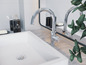 Une salle de bain avec un lavabo blanc, deux robinets chromés et un distributeur de Le Bain.