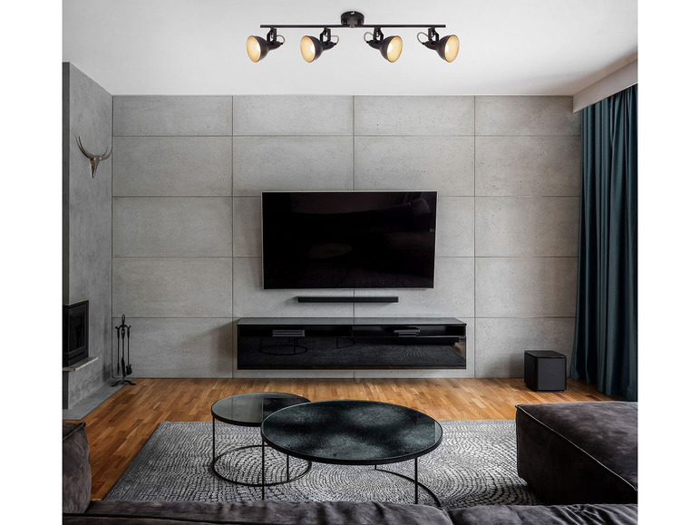 Un luminaire de plafond noir avec quatre ampoules dans un salon moderne.