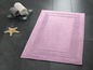 Un tapis de bain rose avec une bordure décorative sur un sol en carrelage noir.