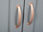 Deux poignées en cuivre sur une armoire en bois gris.