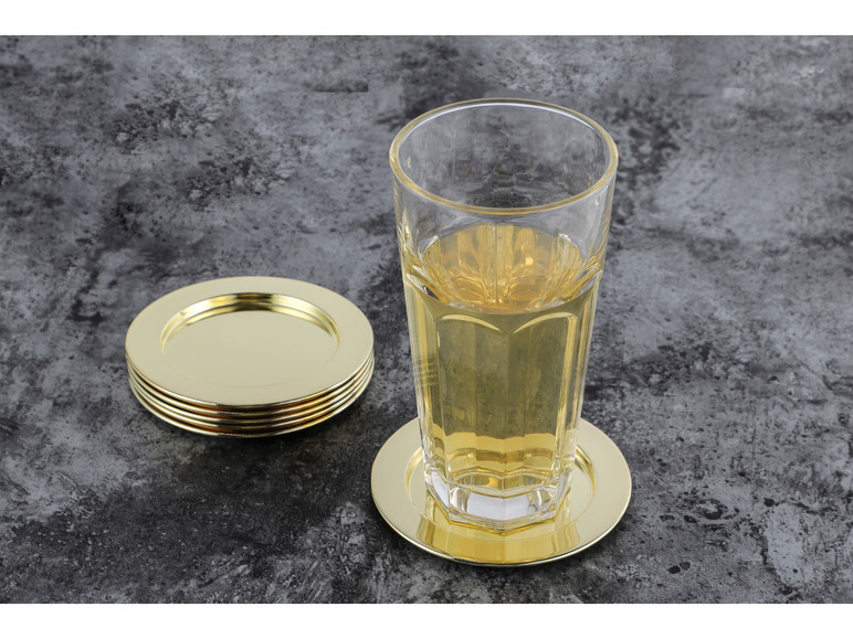 Un verre avec une boisson sur un dessous de verre doré et une pile de dessous de verre dorés.