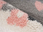 Un tapis rose, gris et blanc avec une texture douce et pelucheuse.