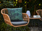 Une chaise en rotin avec un coussin tropical et une table basse assortie.