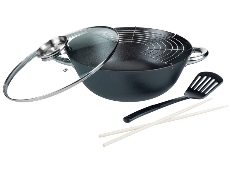 Un wok noir avec un couvercle en verre, un pare-éclaboussures, une spatule et des baguettes.