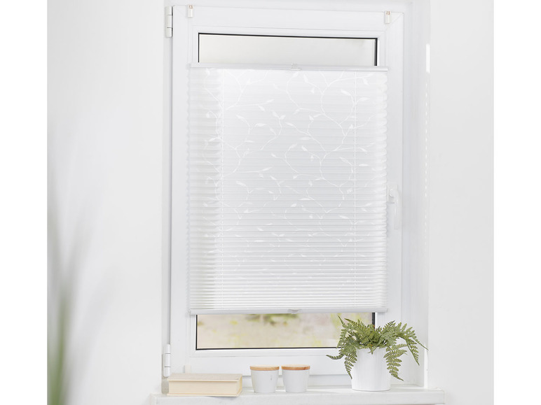 Un store plissé blanc avec un motif de feuilles sur une fenêtre.