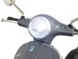 Un gros plan sur le phare d'une Vespa grise.