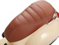 Une selle en cuir marron sur un scooter Vespa crème.