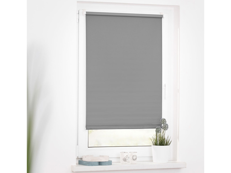 Un store enrouleur gris sur une fenêtre dans un intérieur blanc.