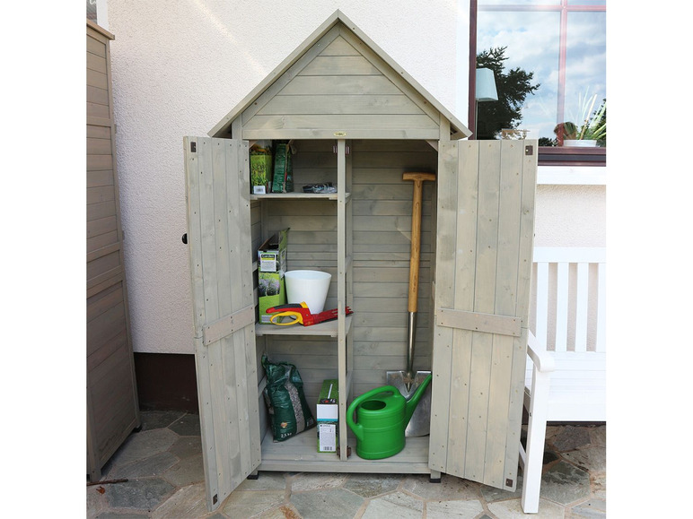 Un abri de jardin en bois avec des outils, un arrosoir et de la terre.