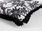 Un coussin blanc avec un imprimé jungle noir et des franges noires.