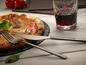 Un couteau et une fourchette à côté d'une pizza avec du jambon et des champignons.