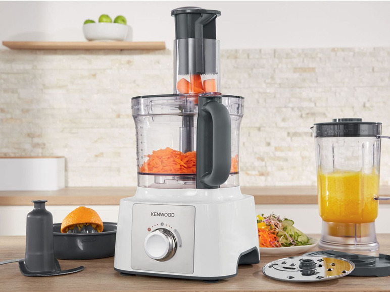 Un robot de cuisine Kenwood avec des carottes coupées, un blender avec du jus d'orange et divers accessoires.