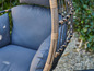 Gros plan d'un fauteuil suspendu en osier avec un coussin gris.