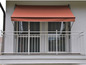 Un balcon avec un store rouge, une balustrade blanche et des fenêtres.