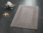 Tapis de bain avec bordure et deux serviettes sur un plateau en verre.