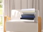 Une pile de linge de lit de différentes couleurs sur un fauteuil.